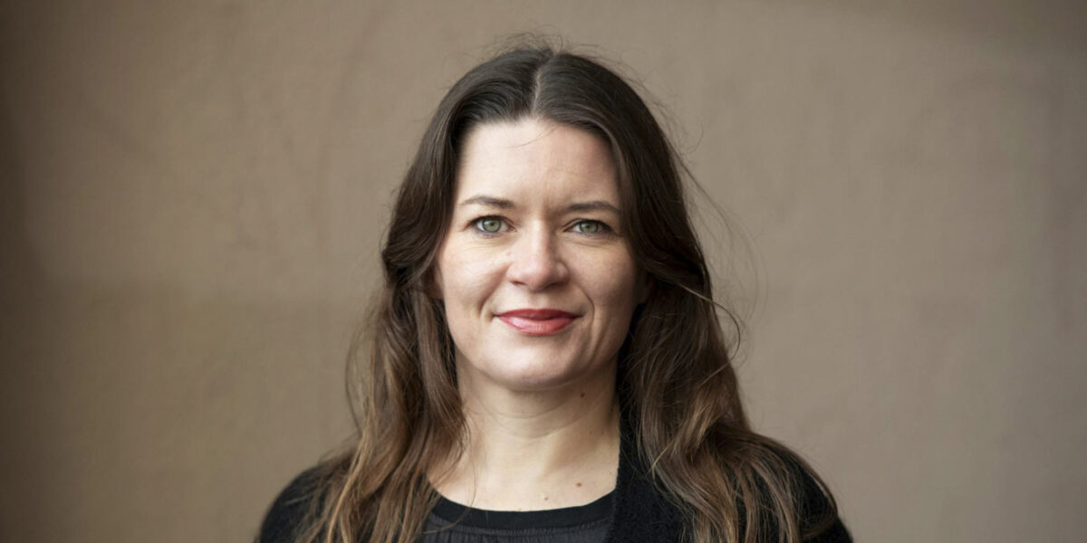 Kvinne står foran en brun vegg.